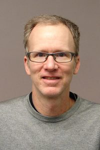 A person wearing glasses and a grey shirt Description automatically generated